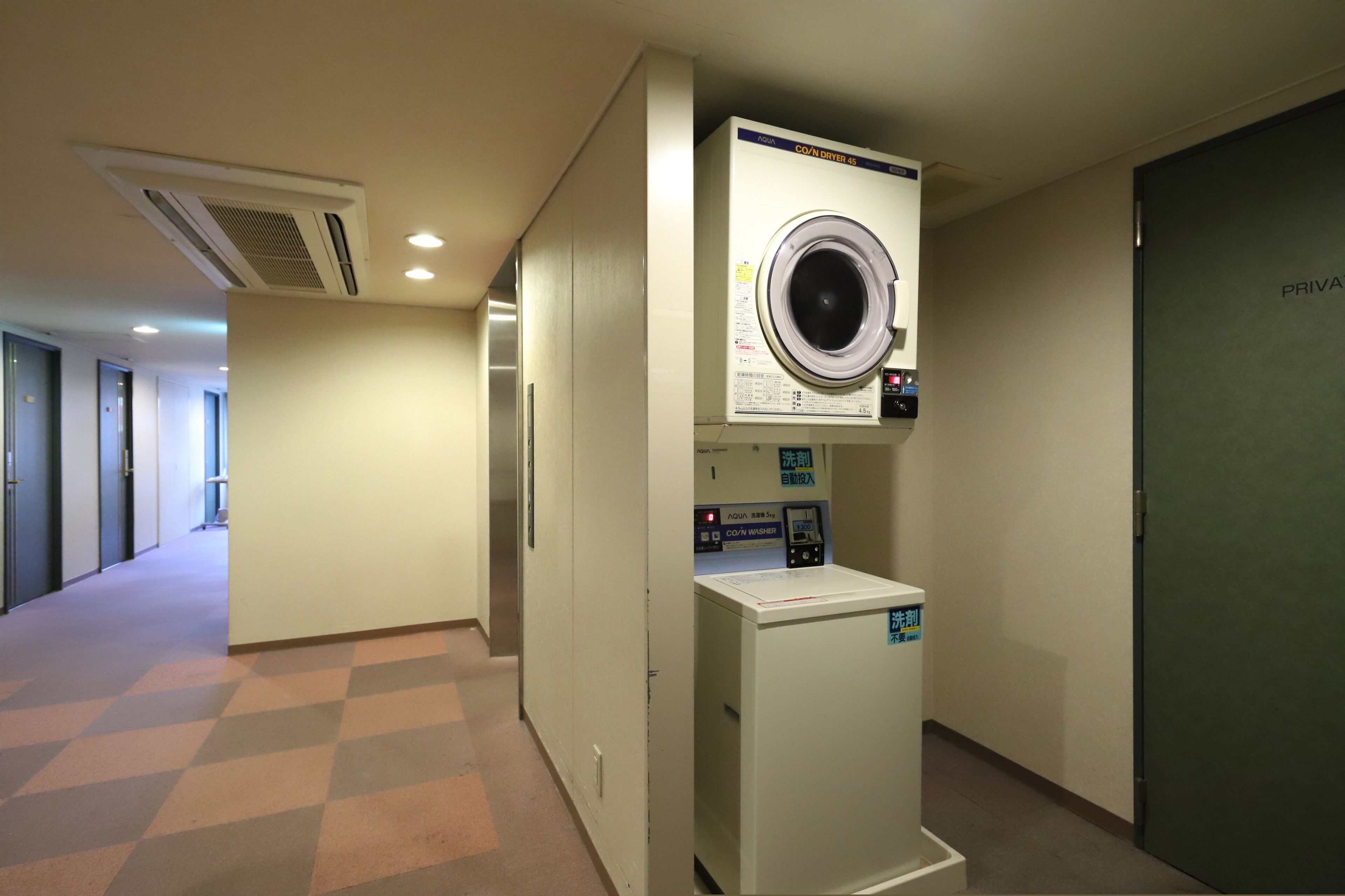 Pasillo de hotel con lavandería que incluye lavadora y secadora de carga frontal, puerta de habitación privada y mostrador de recepción.