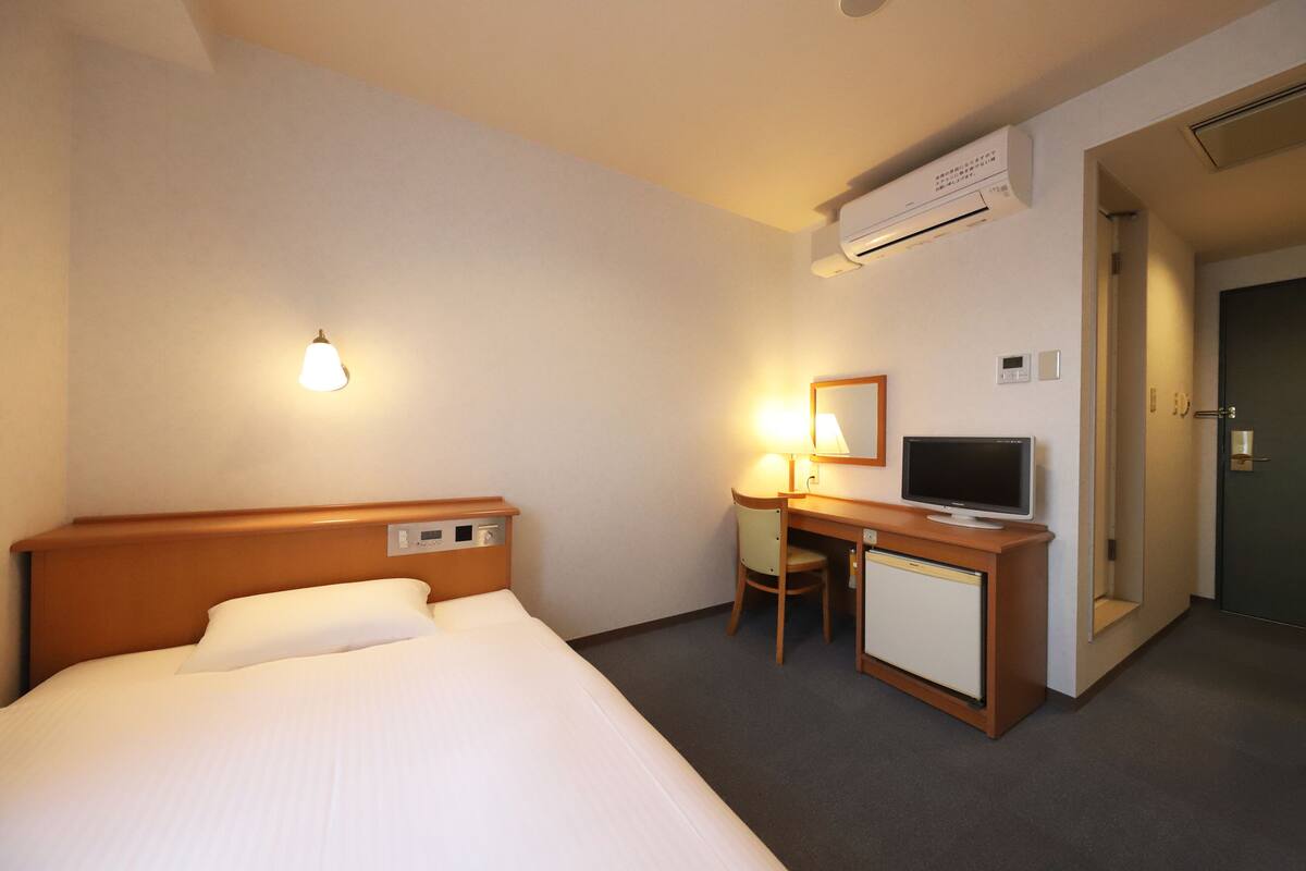 Een hotelkamer met een bed, bureau, stoel, televisie en een airco.