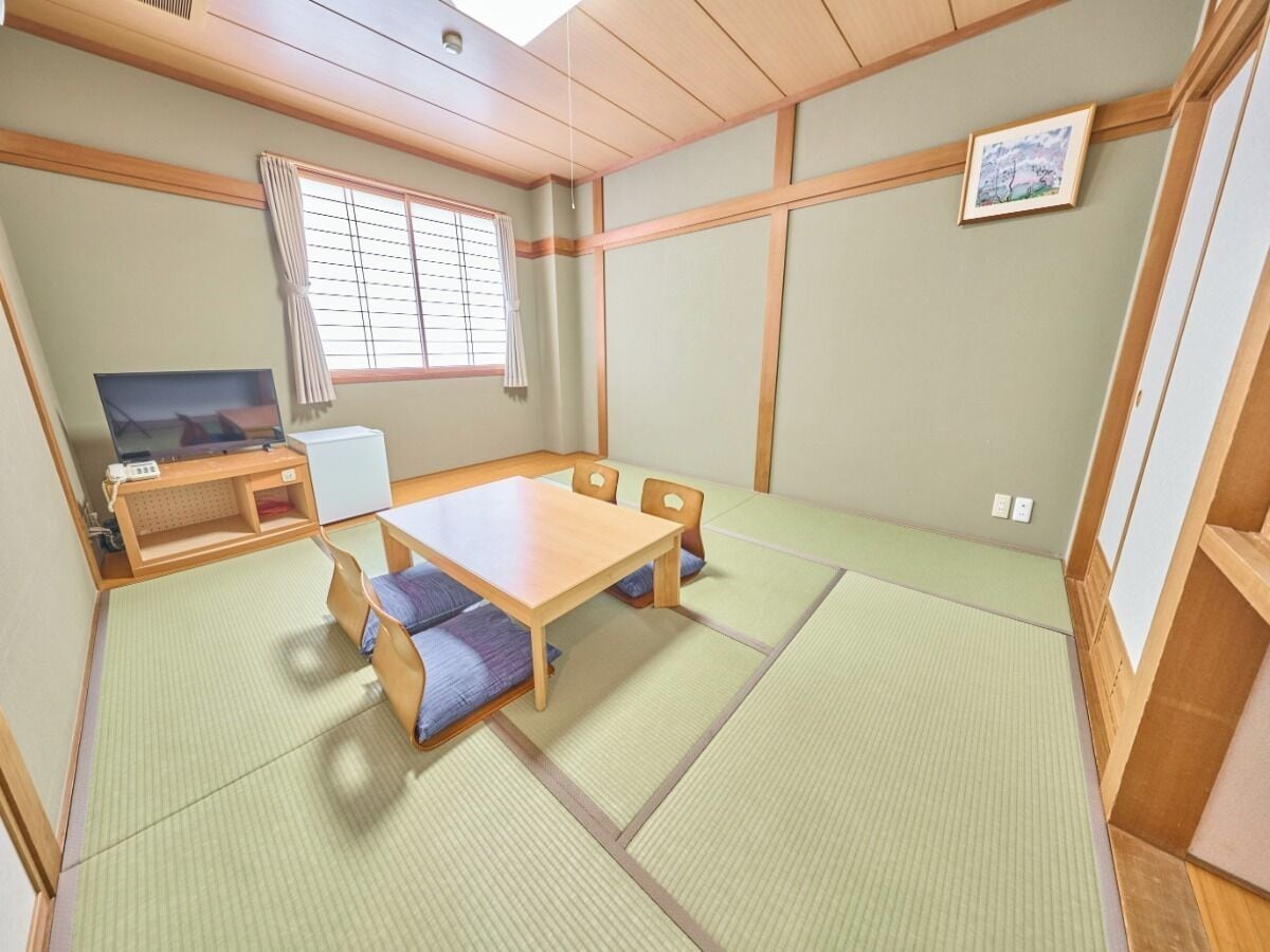 A traditional Japanese room with tatami flooring, a low wooden table, and a television.