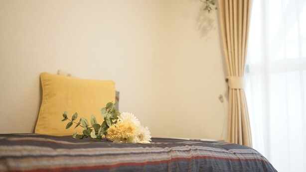 A bed with a striped bedspread, a yellow pillow, and a small floral arrangement. - Santos Heim 103 (Sapporo)