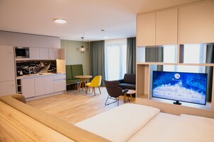 Een moderne hotelkamer met een flatscreen-tv, een bank, een eethoek met tafel en stoelen, en een keuken.