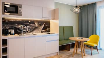 A modern kitchen with a built-in microwave, a sink, and a cityscape mural. There is a green sofa and a yellow chair in the living area.
