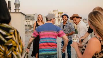 Reunión en una azotea con gente conversando y sosteniendo bebidas, con vistas a un paisaje urbano que incluye edificios y una obra en construcción.