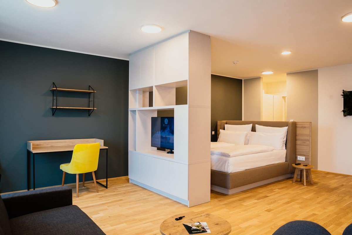 Una habitación de hotel moderna con una cama, un escritorio, una silla y un taburete pequeño.
