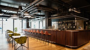 A modern bar area with a wooden counter, multiple bar stools, and a seating area with tables and chairs. - Rioca Vienna Posto 1 (Vienna)