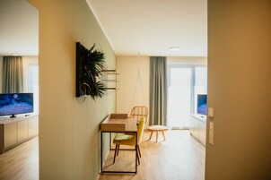 Uma sala de estar moderna com uma mesa de madeira, uma cadeira amarela, uma poltrona suspensa e uma televisão sobre um suporte.