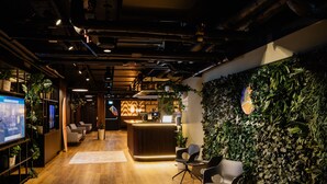 A modern reception area with a wooden floor, a reception desk, and a wall adorned with green foliage. - Rioca Vienna Posto 1 (Vienna)