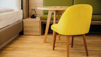 Una habitación con una cama, un sofá verde, un sillón amarillo, una mesita de noche de madera y una mesa redonda de madera.