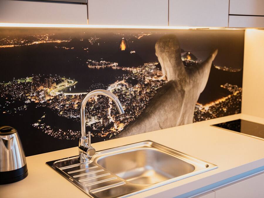 A modern kitchen with a stainless steel sink, a kettle, and a cityscape mural on the backsplash.