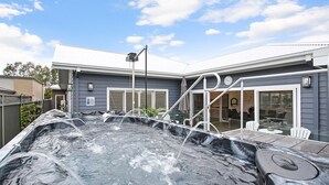 Un área de jacuzzi con terraza techada, un patio con sillas y una casa con garaje al fondo.