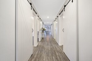A long, narrow hallway with white walls and a wooden floor, leading to a dining area with a chandelier. - The Silver Bull All Abilities (Yarrawonga)