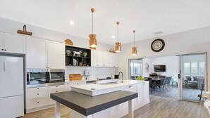 Una cocina moderna con armarios blancos, una isla central, iluminación colgante y un comedor con vistas.