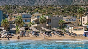 Ein Hotel direkt am Strand mit mehreren Balkonen, Palmen und Liegestühlen.