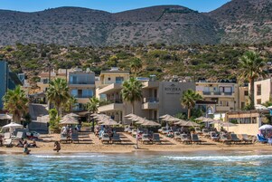 Un hotel frente a la playa con varios balcones, palmeras y sillas de playa.