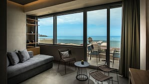 Ein modernes Hotelzimmer mit Balkon und Meerblick, einer Couch, zwei Sesseln und einem kleinen Tisch.