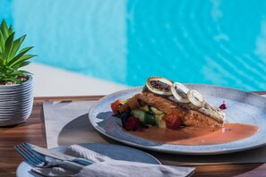 Un plato de comida con pescado, verduras y salsa, sobre una mesa cerca de una piscina.