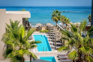 Zona de piscina con sillones de descanso y palmeras, con vista al océano.