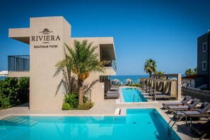 Zona de piscina con sillones de descanso, un cartel que dice 'RIVIERA boutique hotel' y vista al océano.