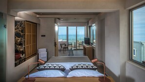 Ein modernes Hotelzimmer mit einem großen Bett, einem Schreibtisch und einem Balkon mit Meerblick.