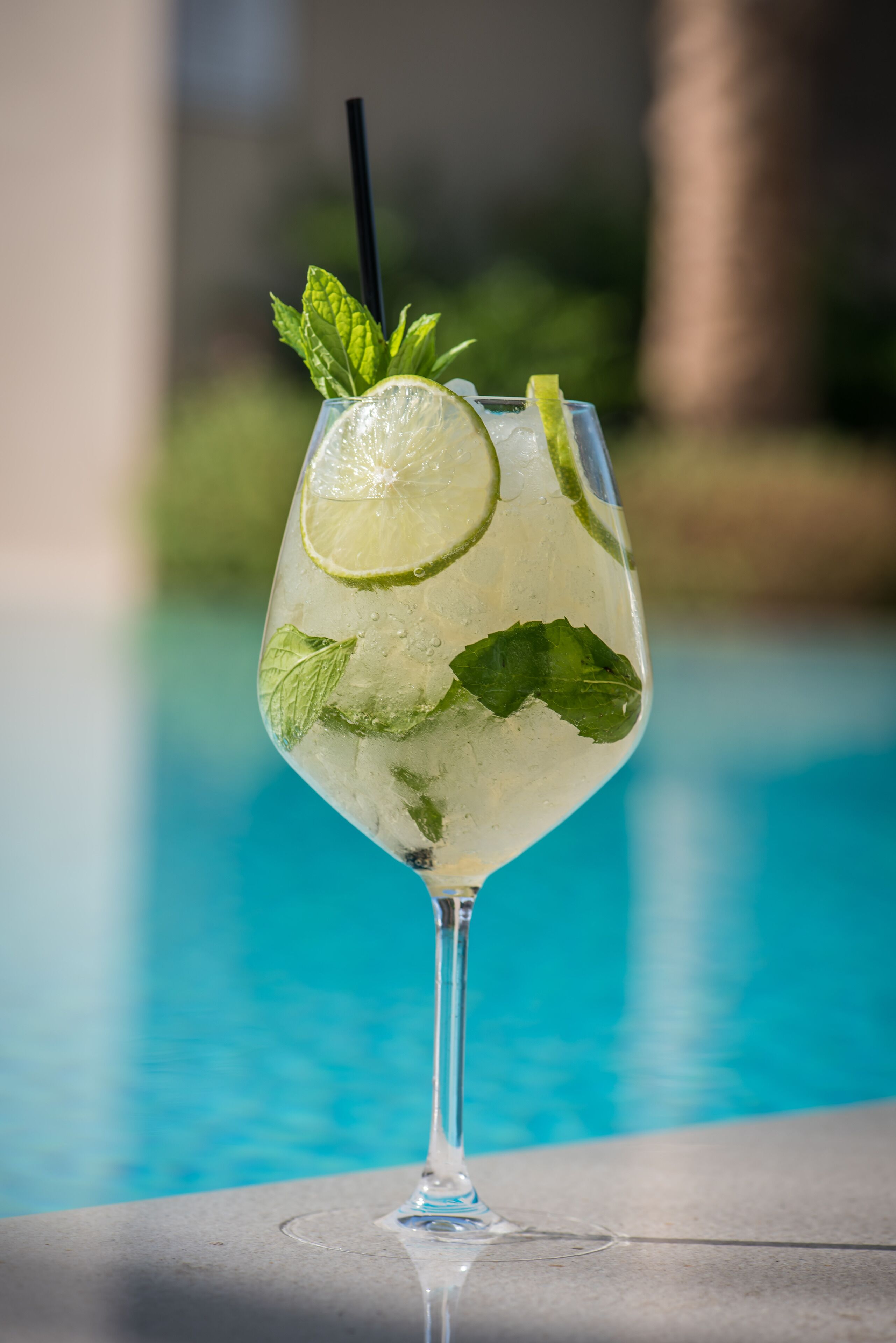 Ein Cocktailglas mit Limette und Minze, platziert auf einer Poolumrandung.