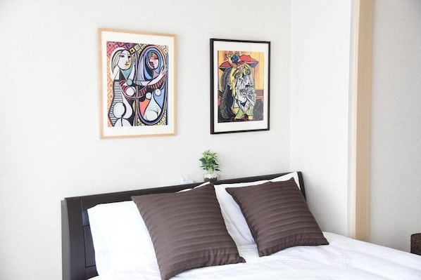 A neatly made bed with two brown pillows and a white comforter. There are two framed artworks on the wall above the bed.