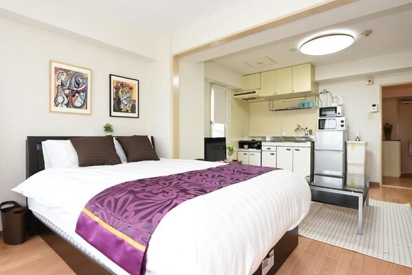 Un dormitorio con una cama grande, una kitchenette pequeña y dos cuadros en la pared.