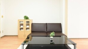 Een woonkamer met een glazen salontafel, een bruine bank en een houten kast met glazen deuren.