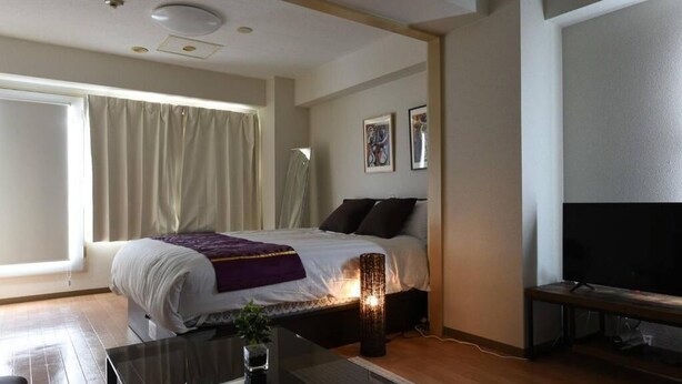 Een moderne slaapkamer met een bed, nachtkastje, lamp en een televisie.