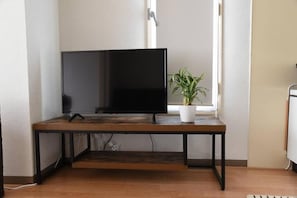 A flat-screen TV on a wooden table with a potted plant beside it.