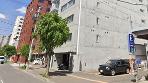 Een meerhoog gebouw met een parkeergarage-ingang, een boom en een heldere lucht.