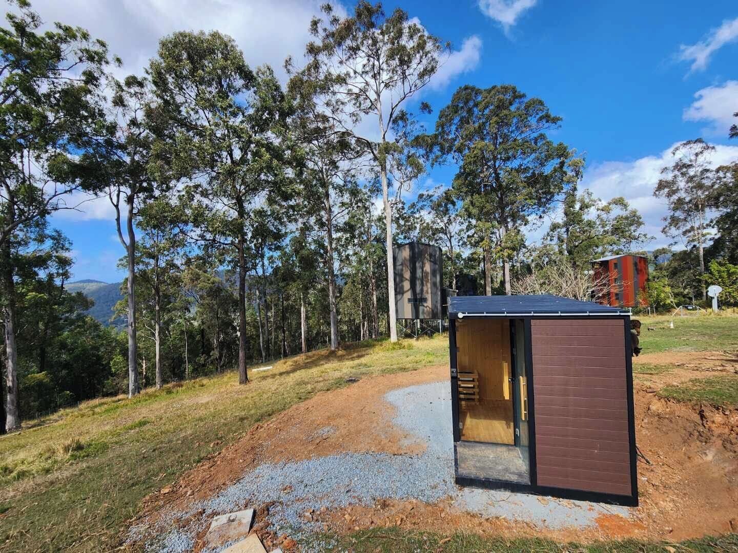 A small wooden structure with a door, surrounded by a gravel path and trees.