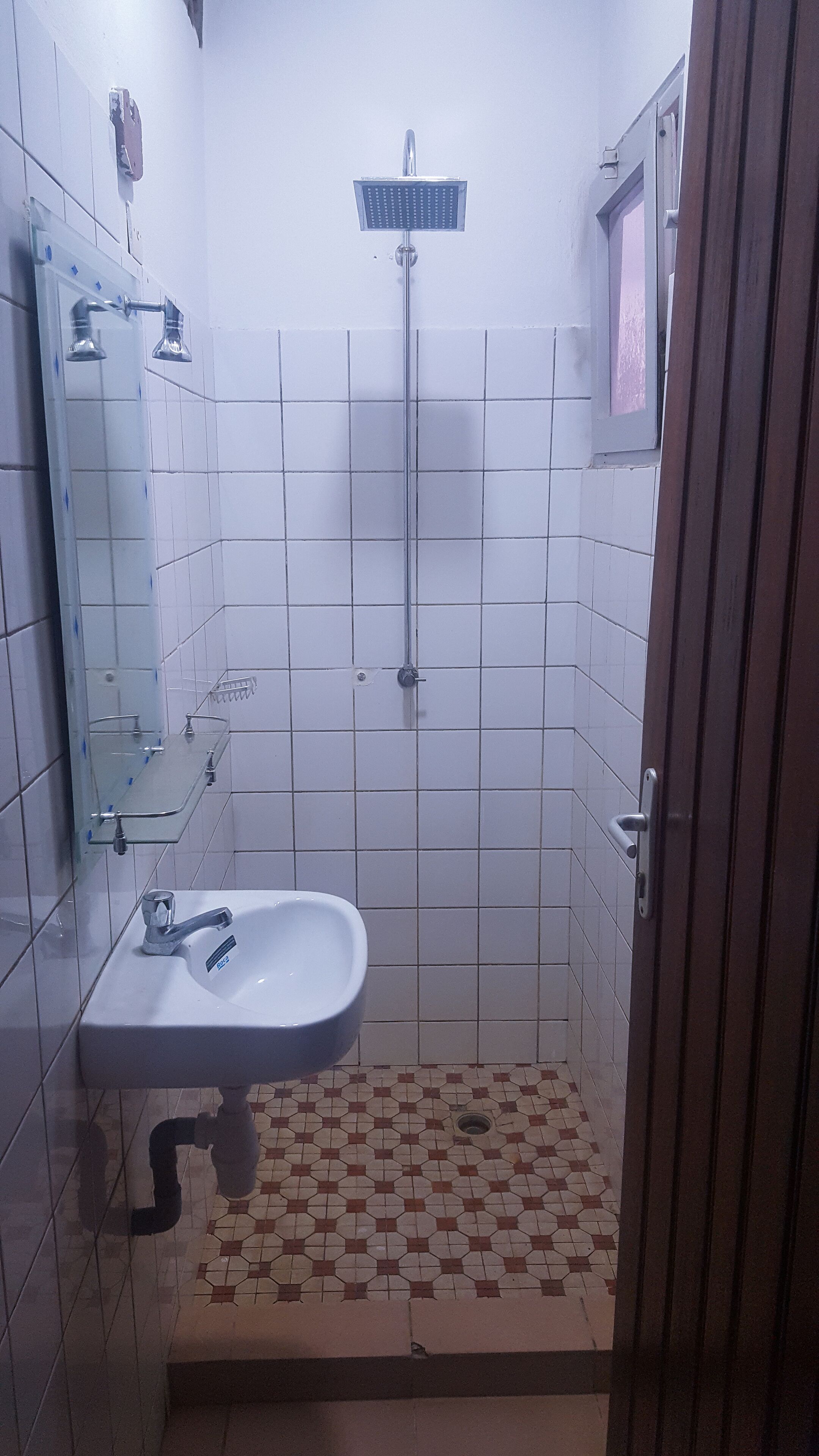 Un baño con lavabo, espejo, ducha y suelo de baldosas.