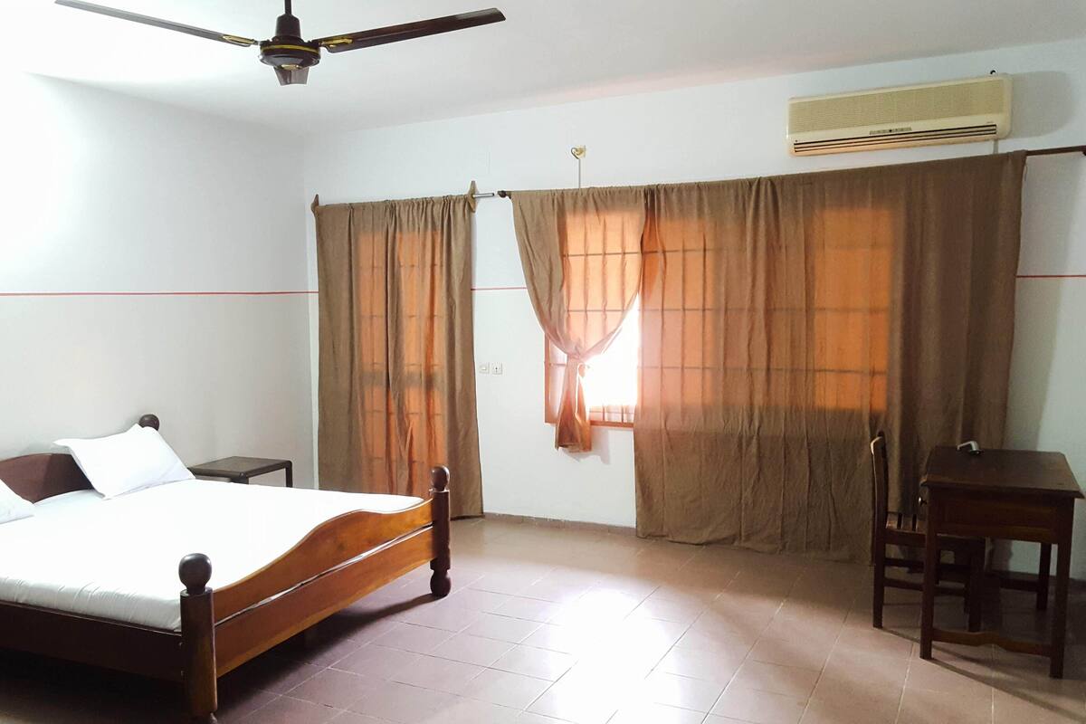 A bedroom with a wooden bed, a desk, a chair, a ceiling fan, and an air conditioning unit.