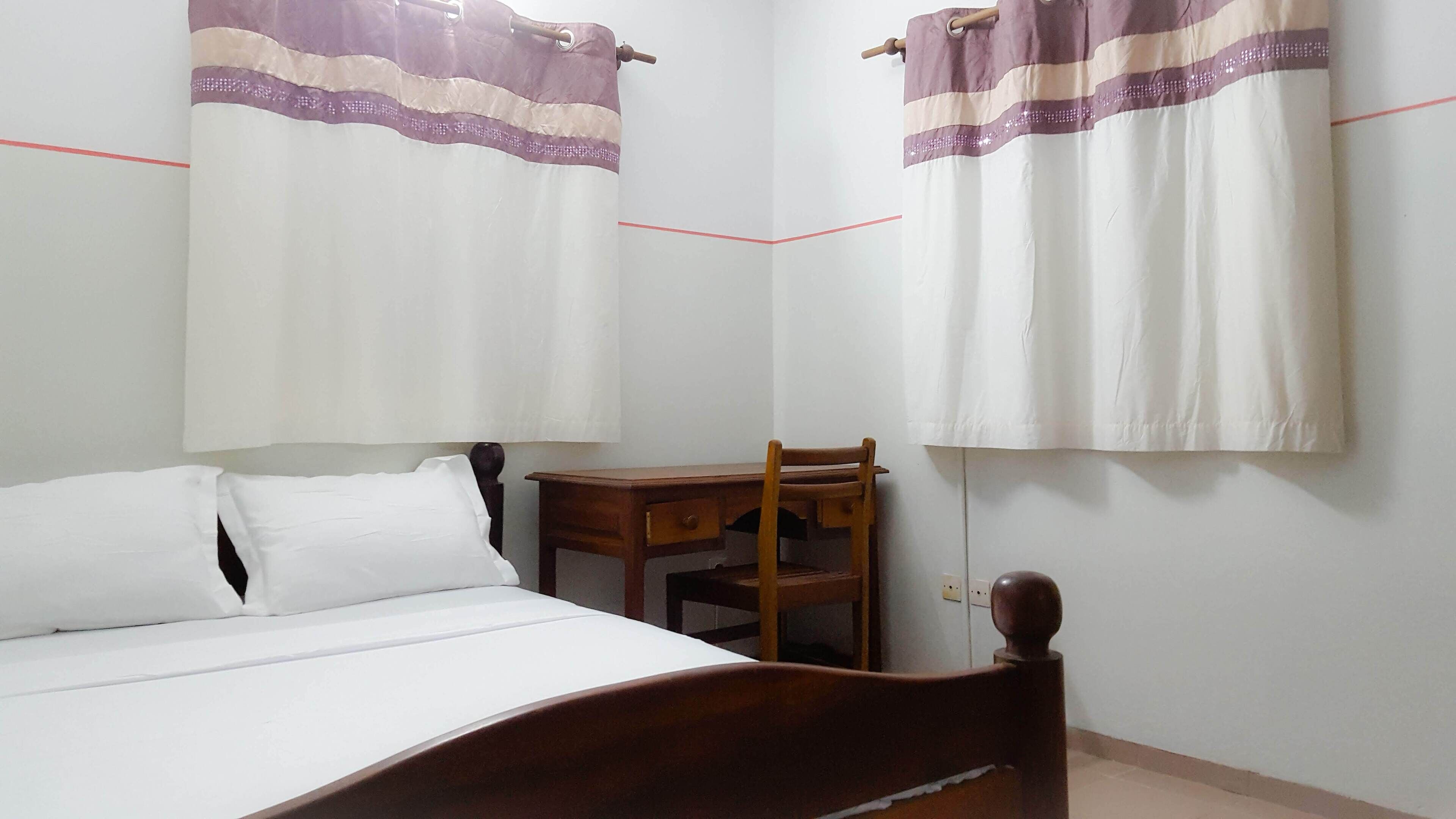 A bedroom with a wooden bed, a small wooden desk, and two curtains with a striped pattern.