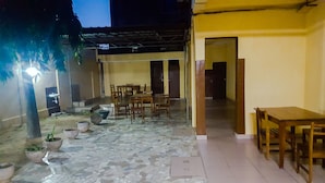 An outdoor patio area with tiled flooring, wooden tables and chairs, potted plants, and a covered seating area. - Academia Hotel (Lomé)