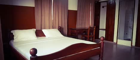A neatly made bed with white linens, a wooden headboard, and a wooden nightstand with a lamp.
