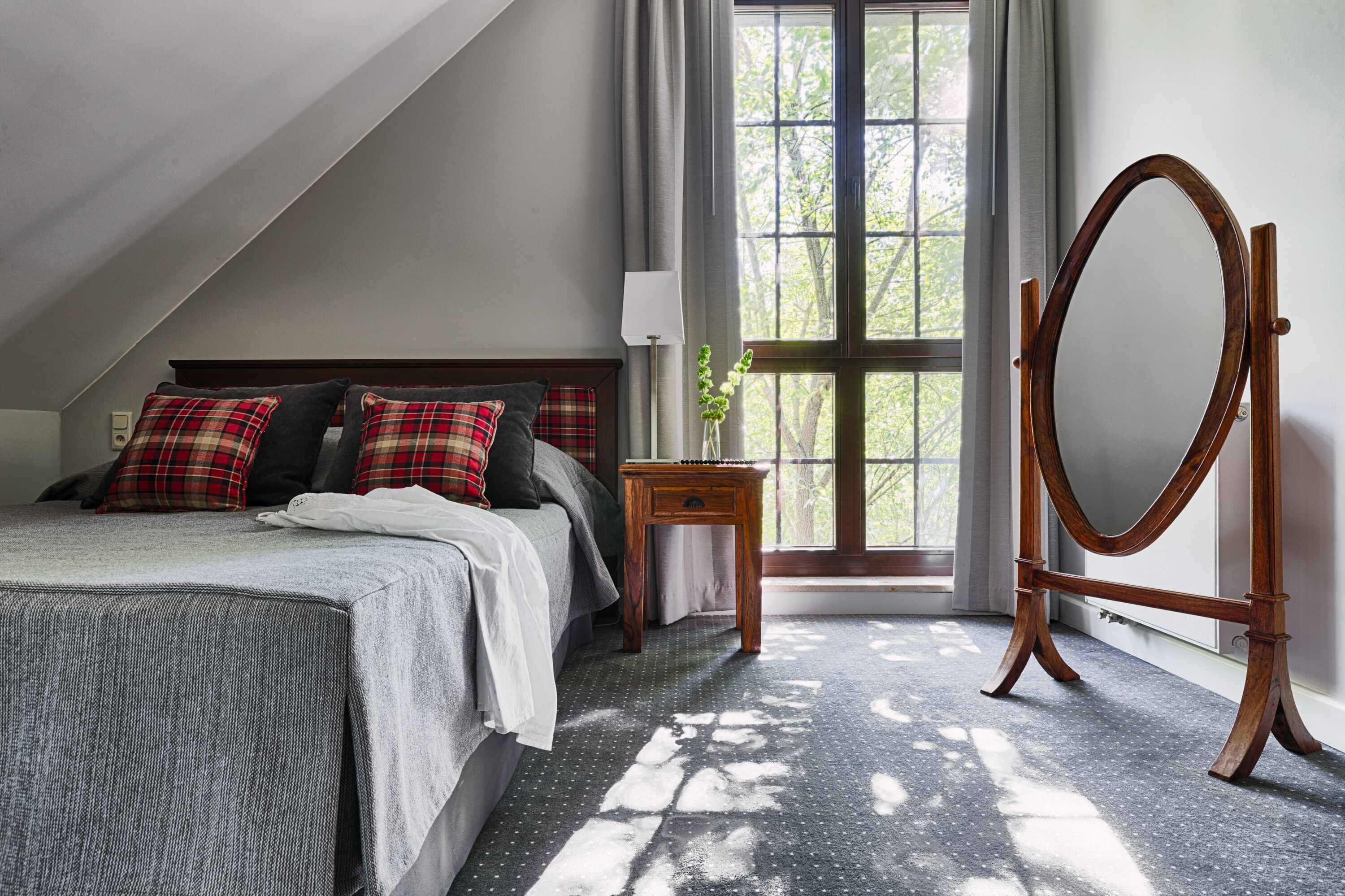 A bedroom with a bed, a wooden dresser, a mirror, and a window with curtains.