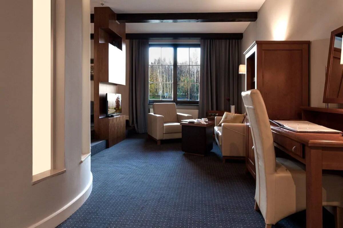 Una habitación de hotel con un ventanal grande, un escritorio, dos sillones, un sofá y una mesita.
