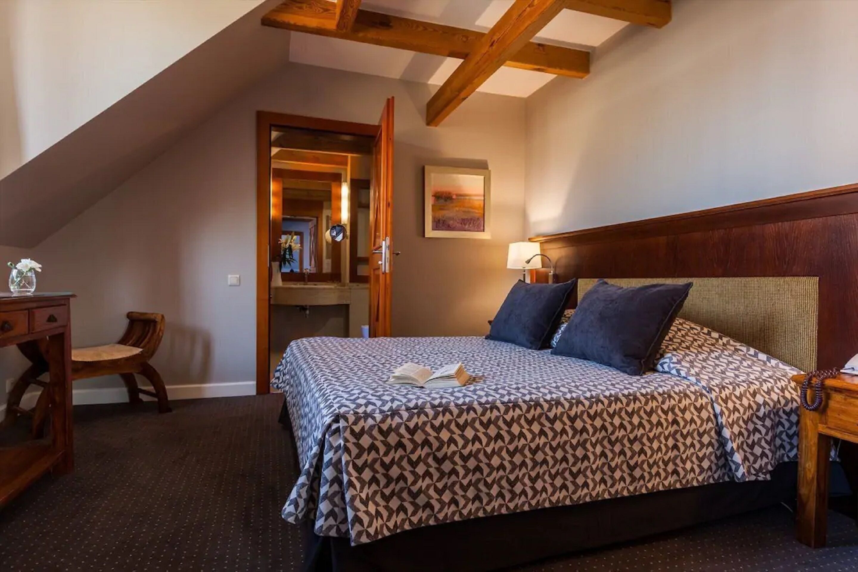 A bedroom with a patterned bedspread, a bedside lamp, and a wooden headboard.