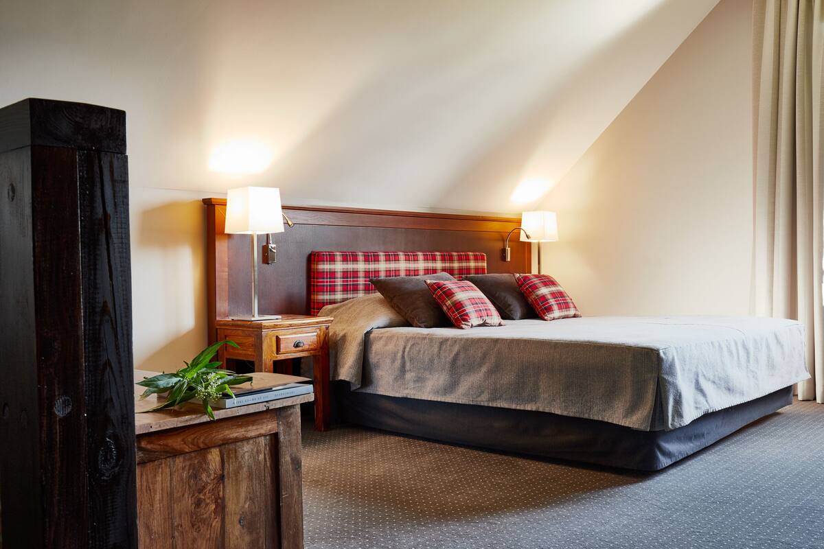 Una habitación de hotel con cama, dos mesitas de noche, una lámpara y un cabecero de madera.
