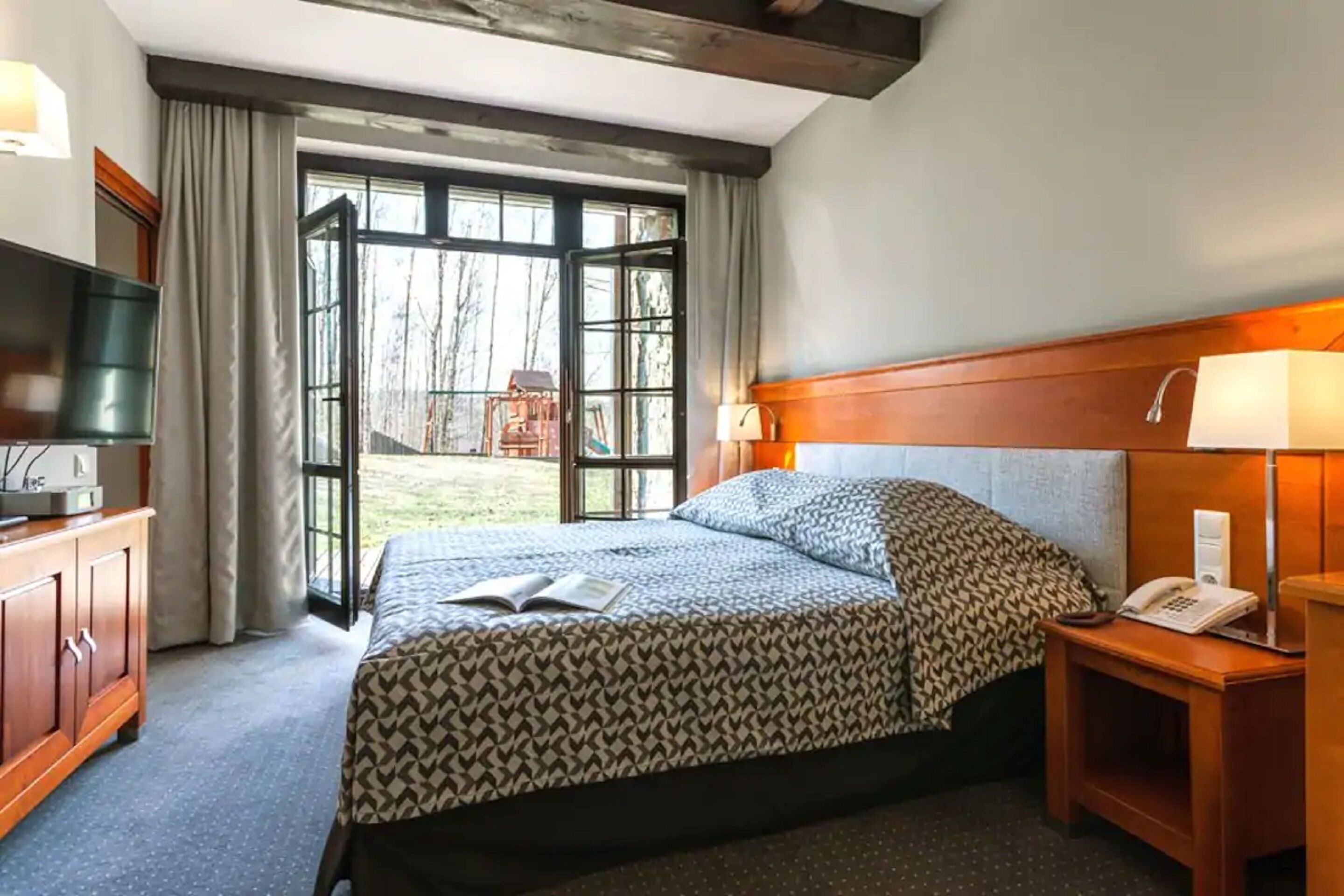 Habitació d'hotel amb un llit gran, una televisió, un escriptori amb una làmpada i vistes a l'exterior a través d'una finestra gran.