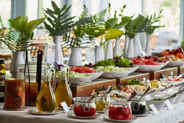 A buffet table with various food items and condiments, including salads, fruits, and beverages, arranged on a table with white tablecloth.