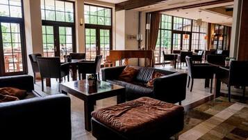 A spacious lobby with a large seating area, a piano, and large windows offering a view of the outdoors.