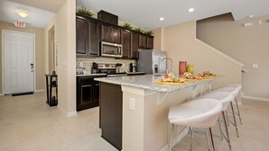 A modern kitchen with dark cabinets, a central island with bar stools, and a microwave above the island. - Family Friendly 4 Bedroom close to Disney in Orlando Area 5126A (Kissimmee)