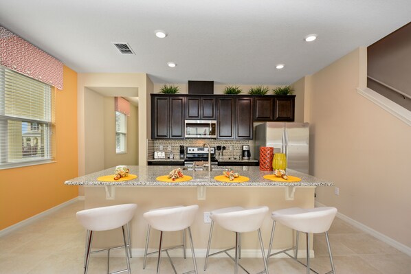 A modern kitchen with dark cabinets, a central island with bar stools, and a large refrigerator.