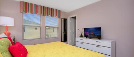 Ein Schlafzimmer mit einem Bett, einem Fernseher, einer Kommode und einem Fenster mit Jalousien.