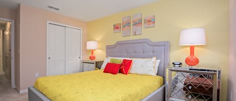 A bedroom with a bed, two bedside tables, a nightstand, a door, and a wall with three paintings.