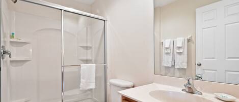 A bathroom with a glass-enclosed shower, a white toilet, a sink with a mirror, and a door with a towel rack.