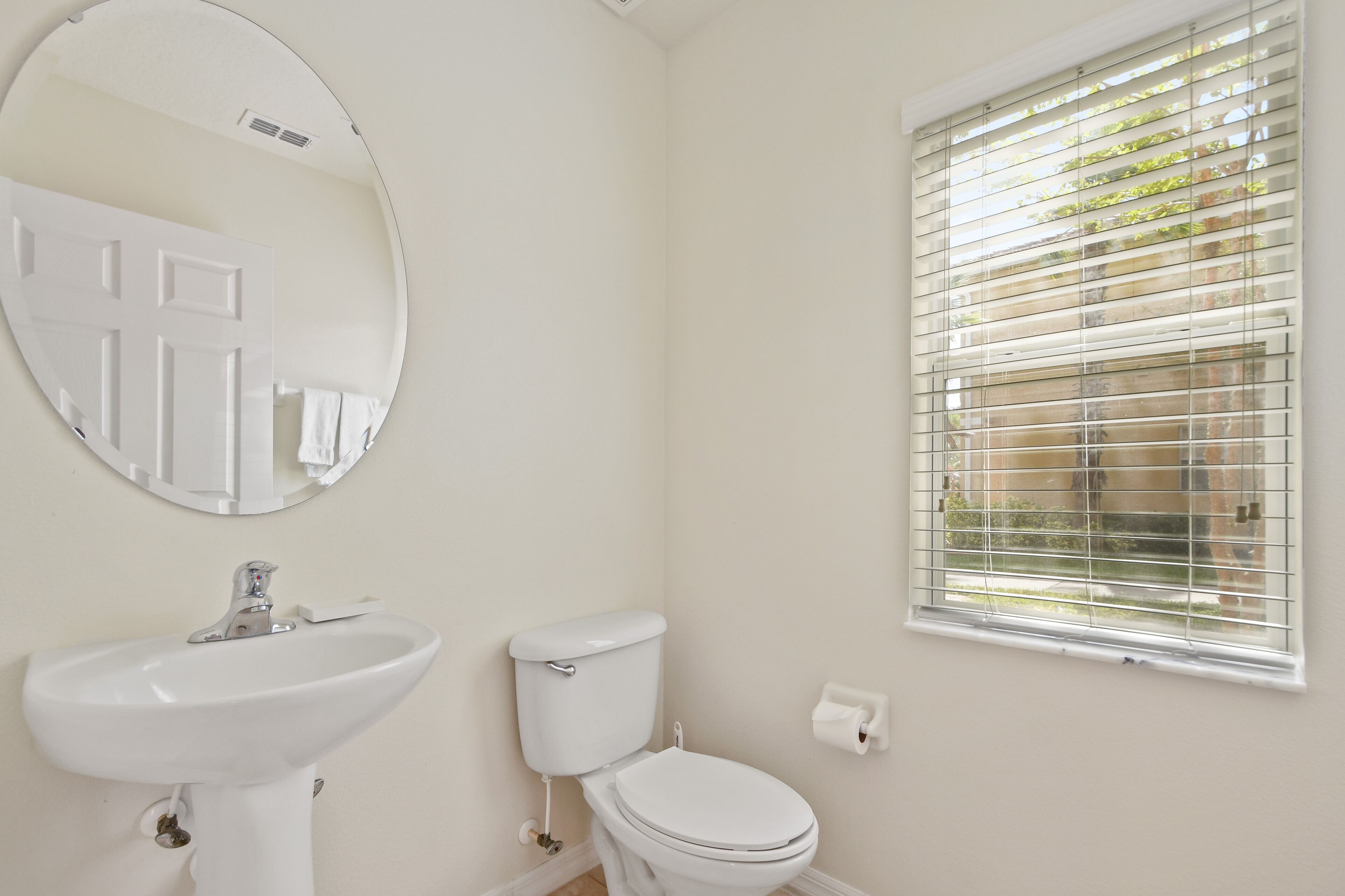 Een badkamer met een wit wastafelmeubel, toilet en een raam met zonwering.