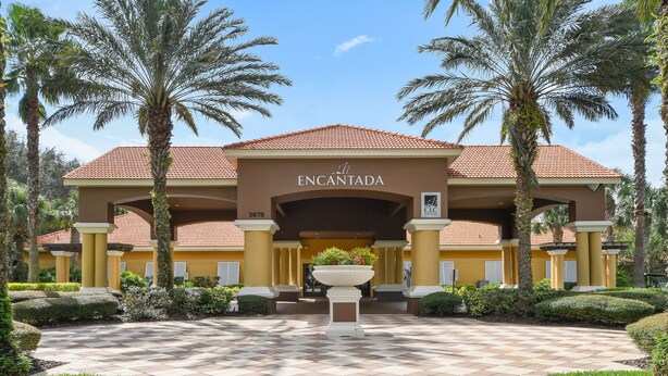 Entrada de hotel con un camino a cuadros, palmeras y una jardinera central.